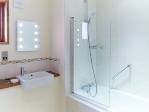 A bathroom with a glass-enclosed shower, a sink with a mirror, and a tiled wall.