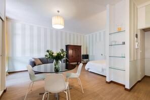 A modern hotel room with a round dining table, white chairs, a sofa, a bed, a wooden cabinet, and a glass shelving unit. - Amazing Duomo loft with terrace and elevator (Florence)