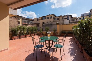 A terrace with a round table and chairs, potted plants, and a view of neighboring buildings. - Amazing Duomo loft with terrace and elevator (Florence)
