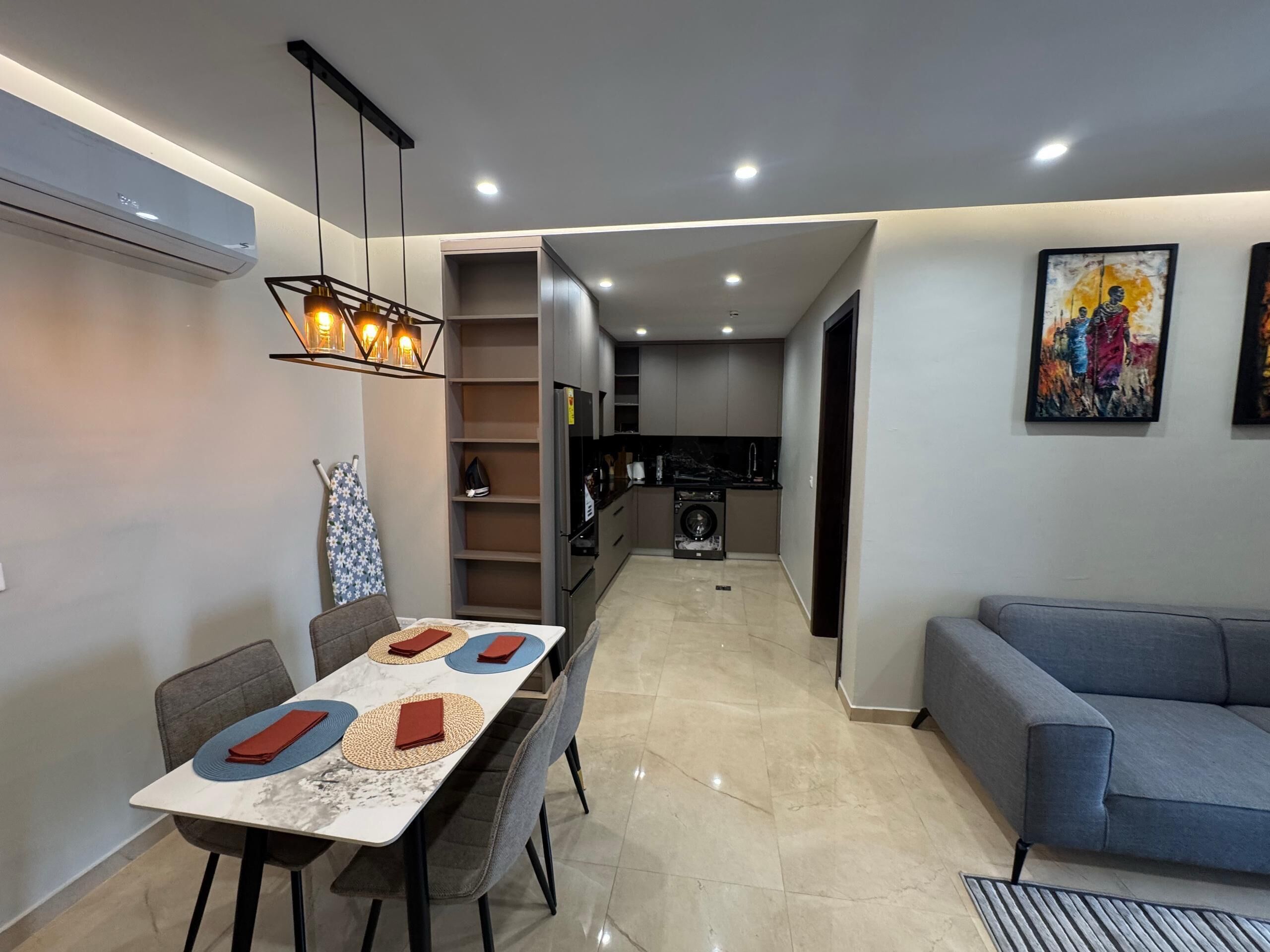 Una cocina moderna con electrodomésticos integrados, un comedor con mesa de mármol y un sofá gris.