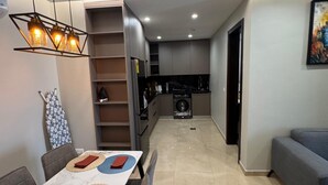 A modern kitchen with a built-in washing machine, a dining area with a table and chairs, and a grey sofa. - Bravia Residence by Cozy (Accra)