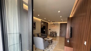 A modern living room with a grey sofa, a small round table, and a TV mounted on a wooden wall. - Bravia Residence by Cozy (Accra)
