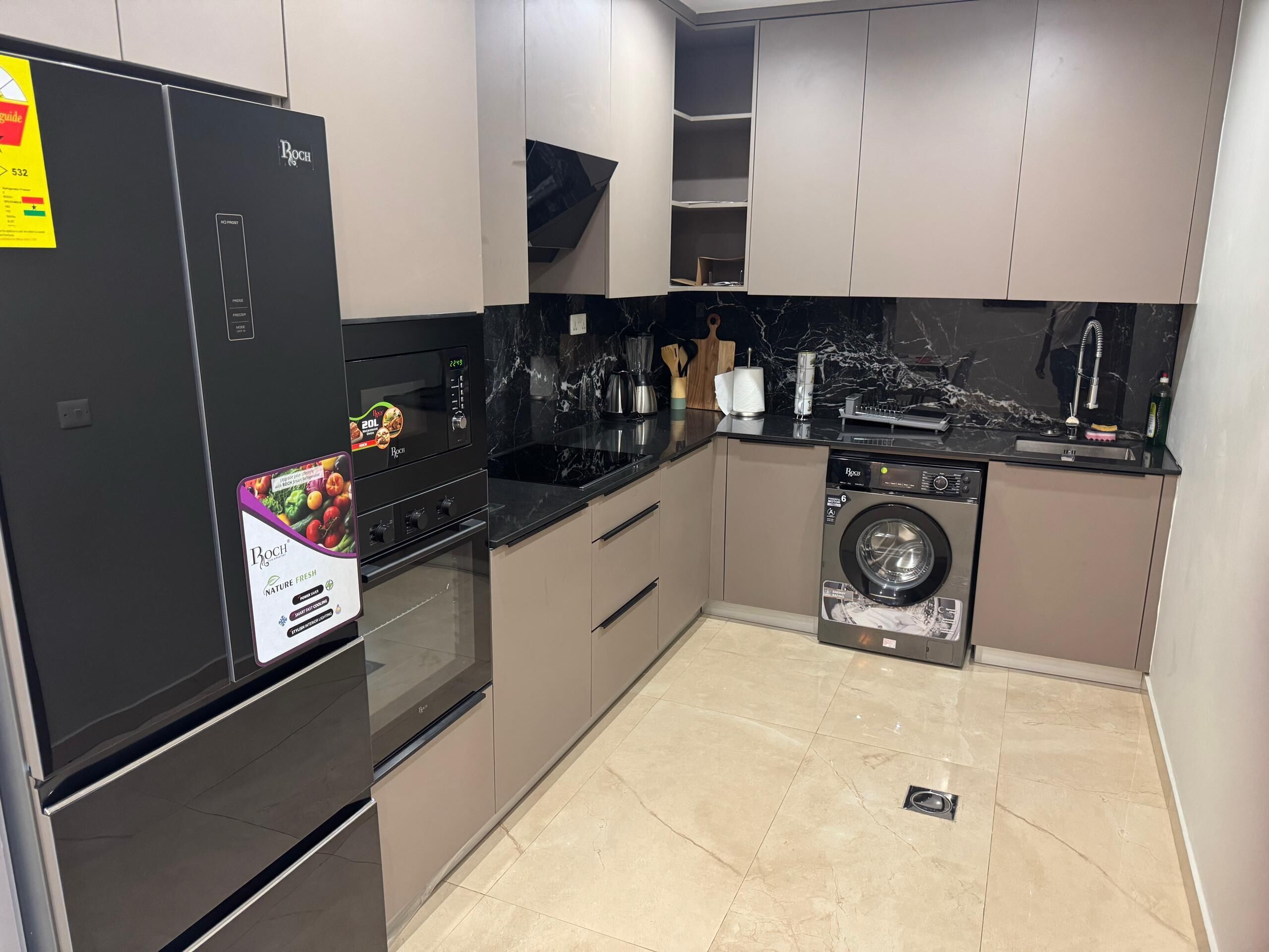 A modern kitchen with a Bosch refrigerator, a built-in oven, a washing machine, and a marble countertop.