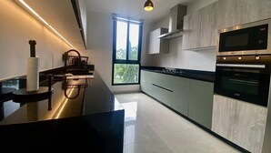 A modern kitchen with a black countertop, stainless steel appliances, and a large window. - Bravia Residence by Cozy (Accra)