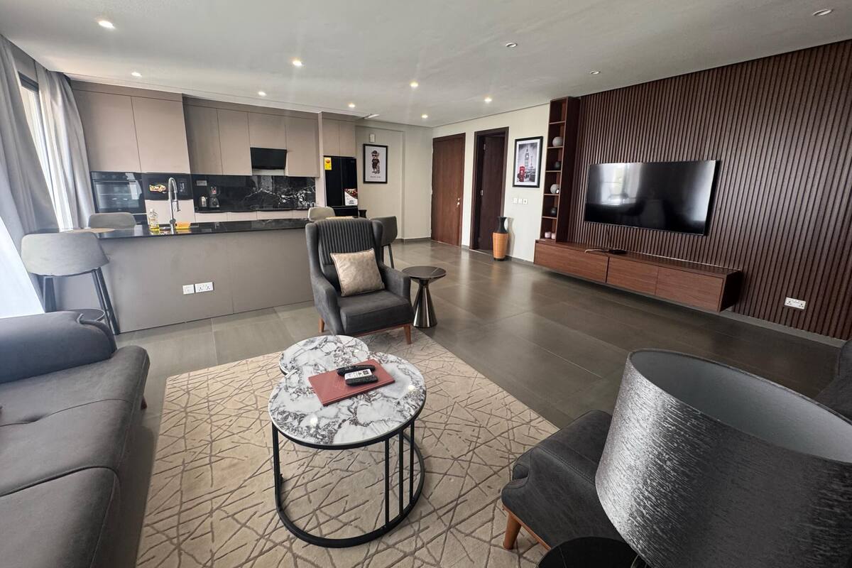 A modern living room with a sofa, armchair, coffee table, and a TV mounted on the wall.