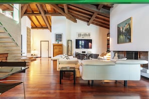 A spacious living area with a wooden ceiling, a fireplace, and a staircase leading to an upper level. - Villa Wanna - Design, Relaxation, and Nature near Milan (Casorate Primo)