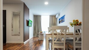 A modern dining area with a wooden floor, white furniture, and a view of the outdoors through large windows. - Wesoła Apartamenty (Wólka Kosowska)