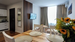 A modern dining area with a wooden table, white chairs, and a vase of sunflowers. - Wesoła Apartamenty (Wólka Kosowska)