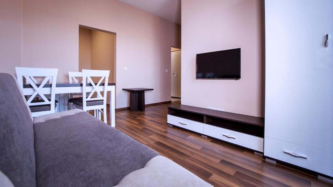 Una sala de estar moderna con sofá, mesa de comedor, sillas, televisor y almacenamiento empotrado.