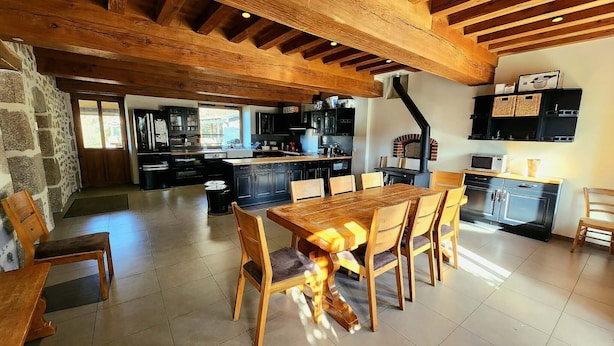 A spacious kitchen with wooden beams, a dining area with a large table, and a stone wall.