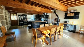 A spacious kitchen with wooden beams, a dining area with a large table, and a stone wall. - Country House “Le Prieuré de Sonne” with Private Terrace and Garden (Lormes)