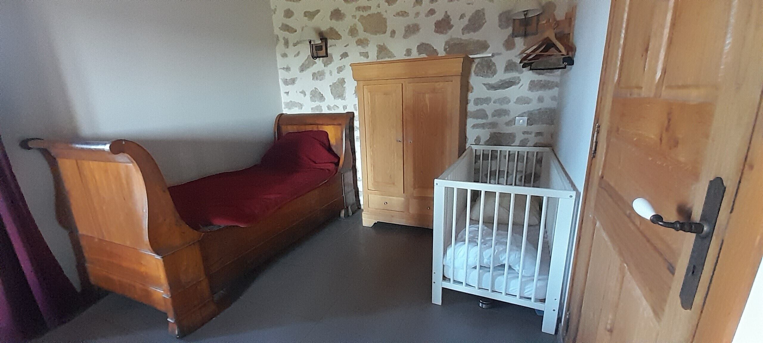 A room with a wooden bed, a white crib, a wooden wardrobe, and a stone-patterned wall.