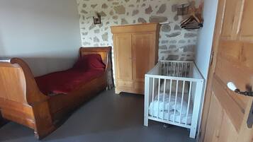 A room with a wooden bed, a white crib, a wooden wardrobe, and a stone-patterned wall.