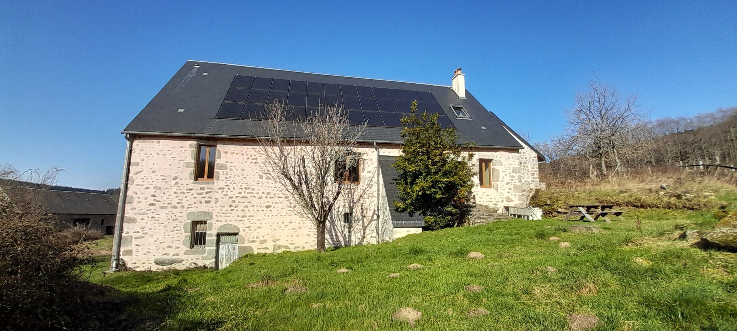 Une maison en pierre avec un toit en pente et des panneaux solaires.