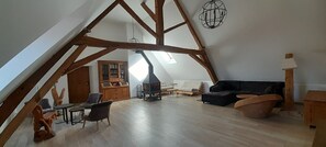 Une pièce de style loft avec des poutres apparentes, une cheminée, un canapé, une table à manger et un buffet.
