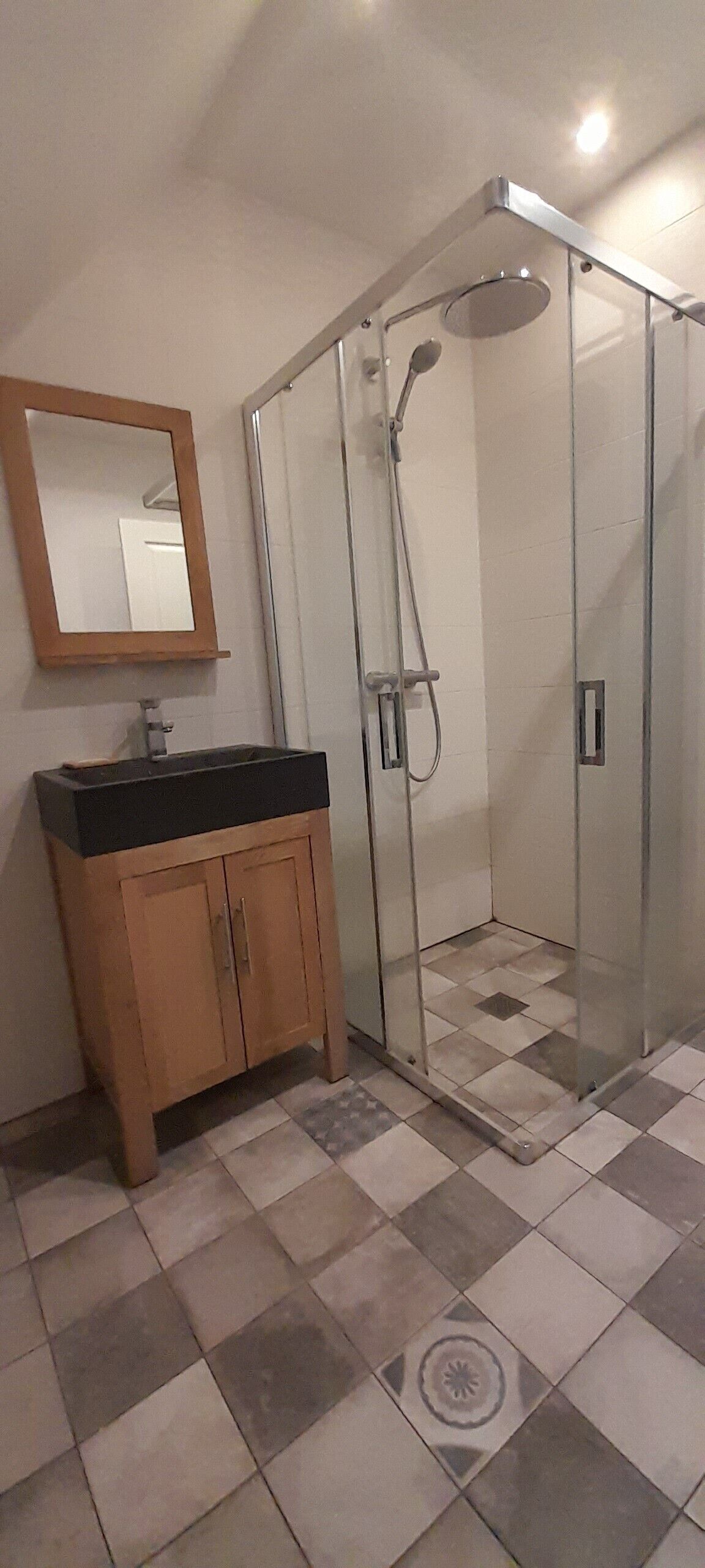 A bathroom with a wooden cabinet, a mirror, and a glass-enclosed shower.