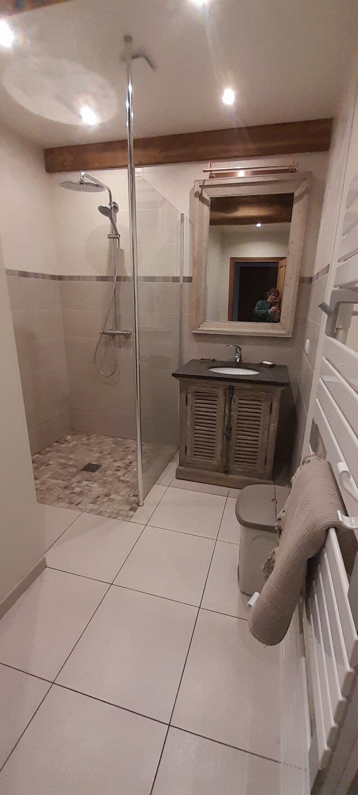 Un baño con ducha envuelta en vidrio, un lavamanos con espejo y un inodoro con toallero.