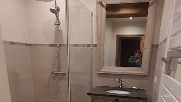 Un baño con ducha envuelta en vidrio, un lavamanos con espejo y un inodoro con toallero.