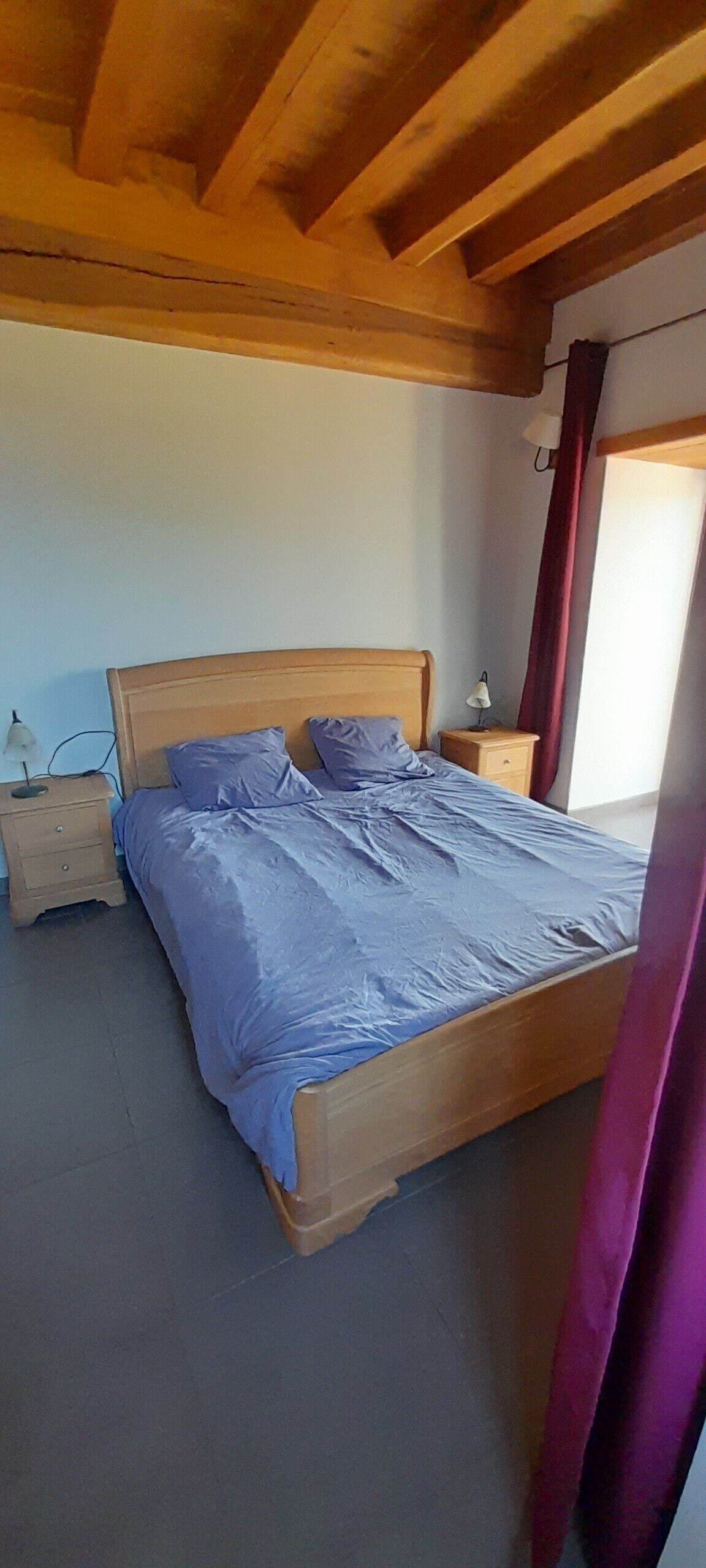 Una camera da letto con un letto di legno, un comodino, una lampada e una finestra con tende.