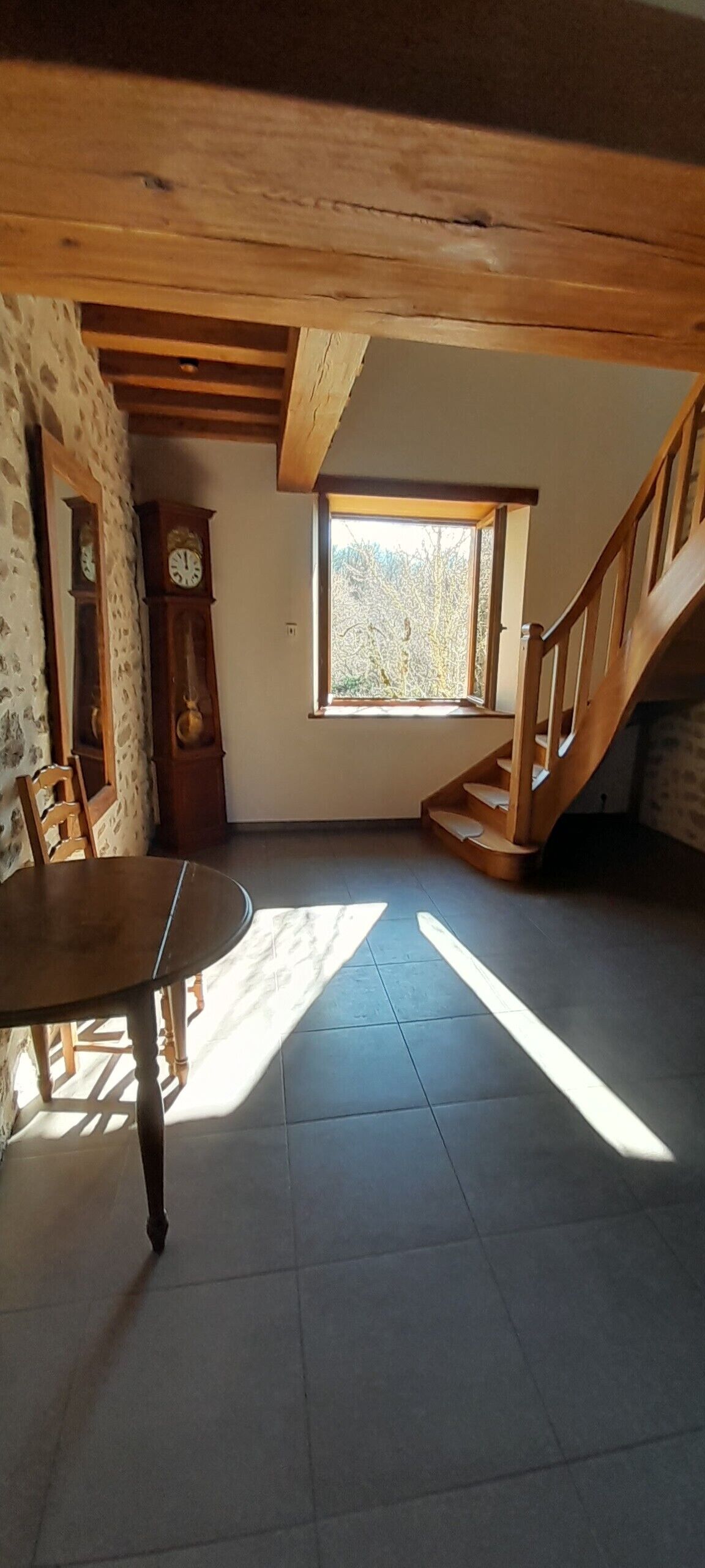 Een kamer met een houten trap, een eettafel en een groot raam.