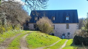 A stone building with a sloped roof, a dirt path leading to it, and surrounding greenery.