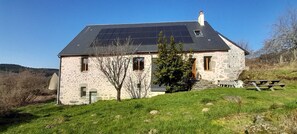 Une maison en pierre avec un toit en pente, des panneaux solaires et une table de pique-nique.