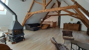 A loft-style room with a wooden beam ceiling, a fireplace, a sofa, a dining table, and a small cabinet.