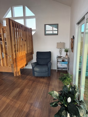 A room with a wooden staircase, a grey armchair, a small table with a lamp and decorative items, and a large potted plant. - Monthly rental  lap pool 40 ft dock wDavitz (Big Pine Key)