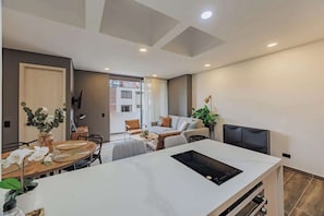 Una sala moderna con comedor, sofá, televisor y un ventanal grande.