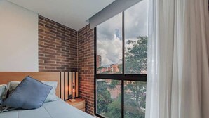 Une chambre avec une grande fenêtre, un mur d’accent en briques et un lit avec des oreillers.