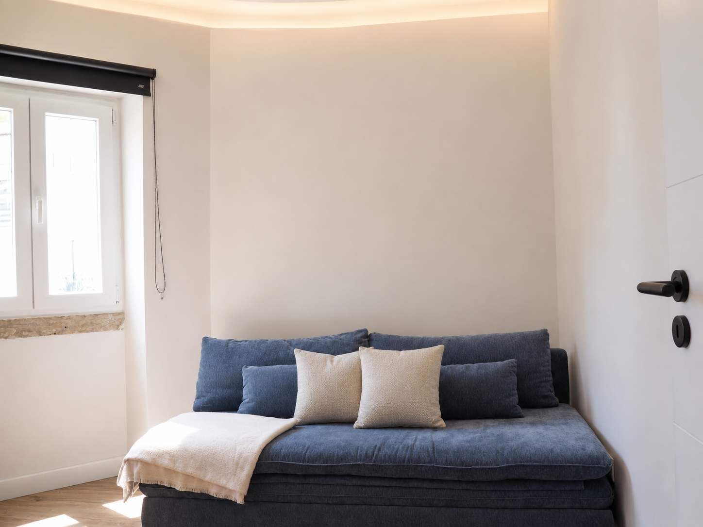 Um quarto com um sofá azul escuro, um cobertor branco e uma janela com persianas.