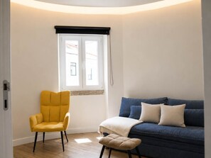 A room with a yellow armchair, a blue sofa, and a window with a black blind. - Spacious Gulbenkian – Families, A/C & Remote Work (Lisboa)