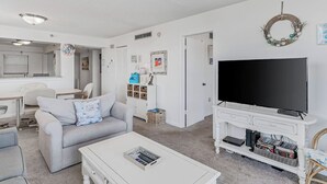 En stue med en hvid sofa, et sofabord, et tv-møbel med et fladskærms-tv og en reol.