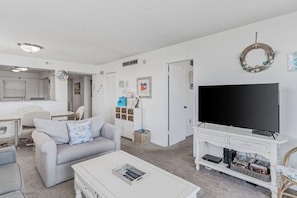 A living room with a white sofa, a coffee table, a TV stand with a flat-screen TV, and a bookshelf. - Gulf Glimpse Getaway • Pool • Steps to Beach (Indian Shores)