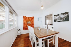 Un coin repas avec une table en bois et des chaises blanches, une tapisserie au mur et une œuvre d’art en noir et blanc.