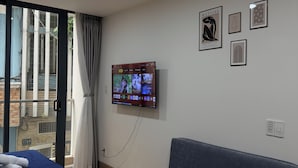 Quarto de hotel com cama, sofá, televisão na parede e janela com cortinas.