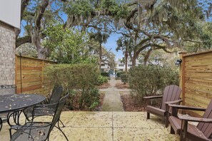A patio with a round table and chairs, surrounded by wooden fences and trees with hanging moss. - A Bit of Hope Island Townhouse, Close to Beach and Community Pool (Saint Simons Island)