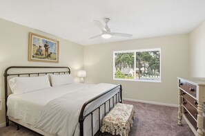 A bedroom with a bed, a nightstand, a dresser, a ceiling fan, a window with blinds, and a painting on the wall. - A Bit of Hope Island Townhouse, Close to Beach and Community Pool (Saint Simons Island)