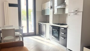 A modern kitchen with a dining area, a sofa, and a sliding glass door leading to a balcony. - PP08 - Porto Potenza, two-room apartment with garden, 100 meters from the sea (Potenza Picena)