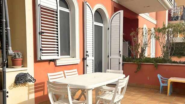 A patio with a white table and chairs, a potted plant, and a door with shutters. - PP08 - Porto Potenza, two-room apartment with garden, 100 meters from the sea (Potenza Picena)