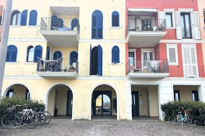 A multi-story building with balconies, arched doorways, and bicycles parked in front. - PP08 - Porto Potenza, two-room apartment with garden, 100 meters from the sea (Potenza Picena)