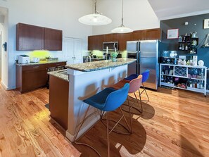 A modern kitchen with wooden cabinets, a central island with bar stools, a refrigerator, and a microwave.