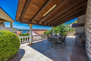 Une terrasse extérieure dotée d’une pergola en bois, d’une table ronde avec des chaises et d’un mur en pierre.