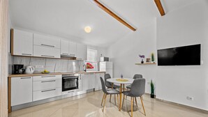 A modern kitchen with white cabinets, a dining area with a round table and chairs, and a flat-screen TV mounted on the wall. - Two Bedroom Apt near the Beach - Villa Jagoda (Kampor)
