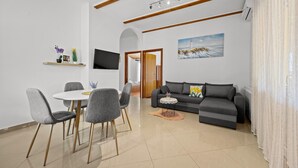 A modern living room with a dining area, a gray sofa, a flat-screen TV, and a painting of a lighthouse. - Two Bedroom Apt near the Beach - Villa Jagoda (Kampor)
