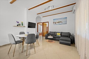 Ein modernes Wohnzimmer mit Essbereich, einem grauen Sofa, einem Flachbildfernseher und einem Gemälde eines Leuchtturms.