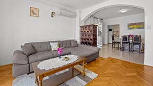 A living room with a grey sofa, wooden coffee table, and a dining area with wooden chairs and a table. - Four Bedroom Apt. near the Beach - Villa Jagoda (Kampor)
