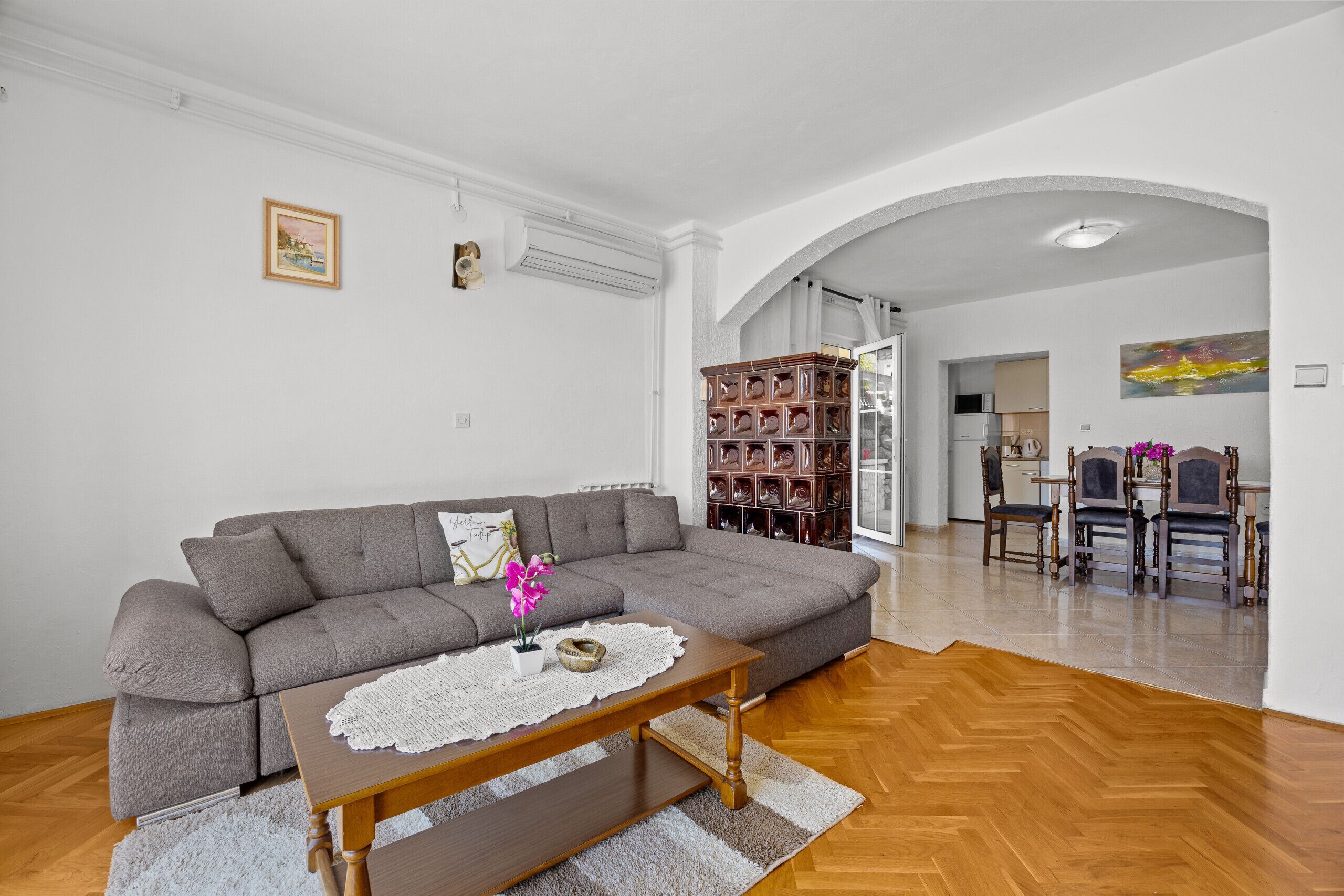 Ein Wohnzimmer mit grauem Sofa, Couchtisch aus Holz und einem Essbereich mit Holzsesseln und Tisch.