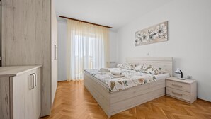 A bedroom with a wooden wardrobe, a bed with floral bedding, a bedside table, and a wall-mounted artwork. - Four Bedroom Apt. near the Beach - Villa Jagoda (Kampor)