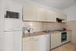 Eine Küchenzeile mit weißem Kühlschrank, Mikrowelle, Kaffeemaschine, Wasserkocher, Spüle und Backofen.